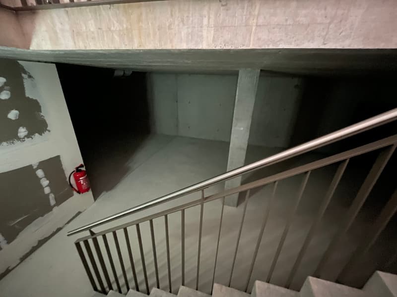 Concrete staircase, metal handrail, white ceiling, garage with walls and a concrete floor