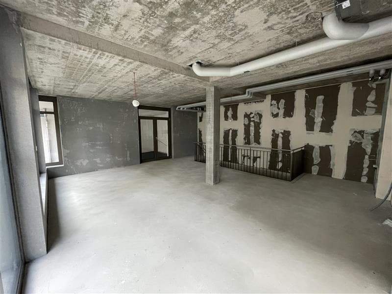 A room with grey walls and flooring, a staircase, and pipework