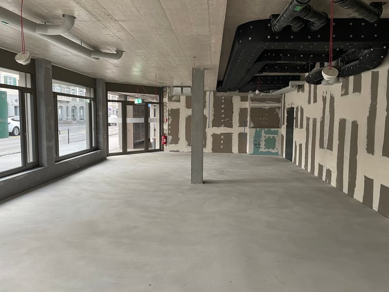 A large empty room with unfinished walls and columns, two doors to the street, windows