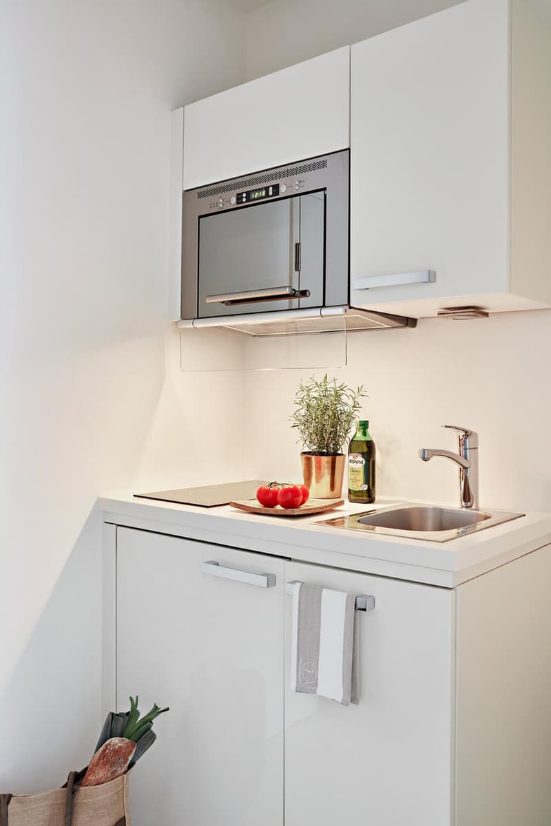 Modern white kitchen with cabinets, induction stove, oven, sink, microwave, plants, and utensils