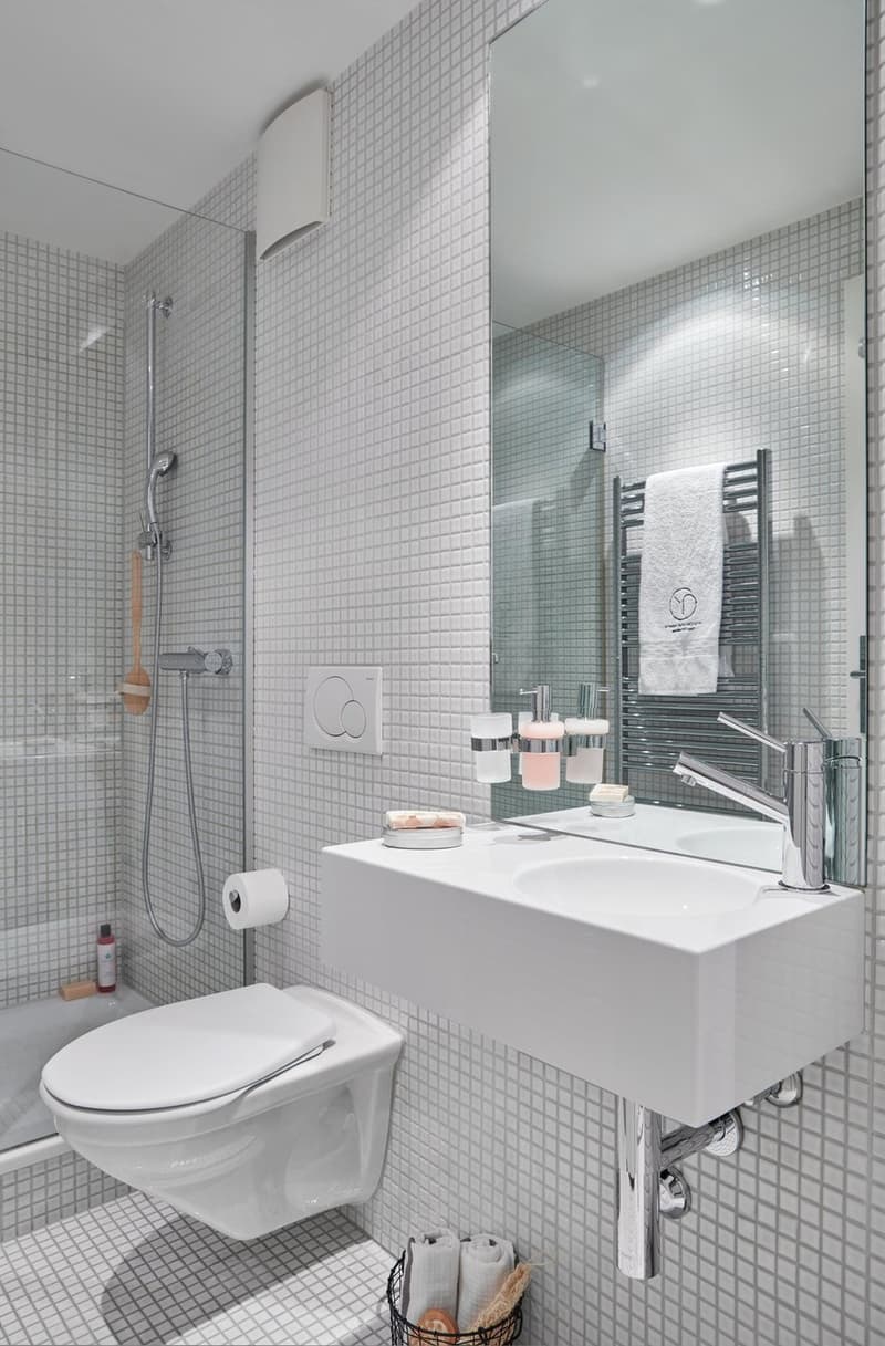 white tile wall, white ceramic sink, white toilet, shower head, towel rack, basket with towels