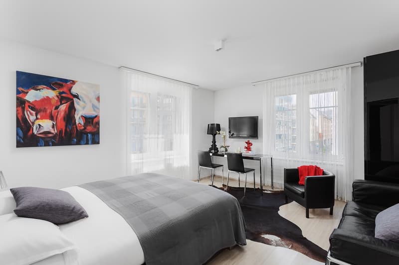 Modern and minimalist bedroom with white walls, wooden floor, large windows with white curtains, double bed, modern nightstand, TV, desk, and a chair