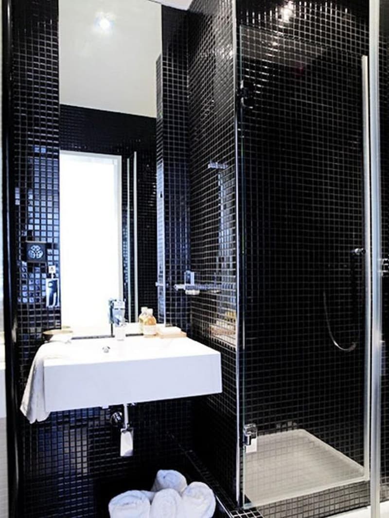 white tiled walls, black tiled floors, white bathtub, white sink, glass shower enclosure