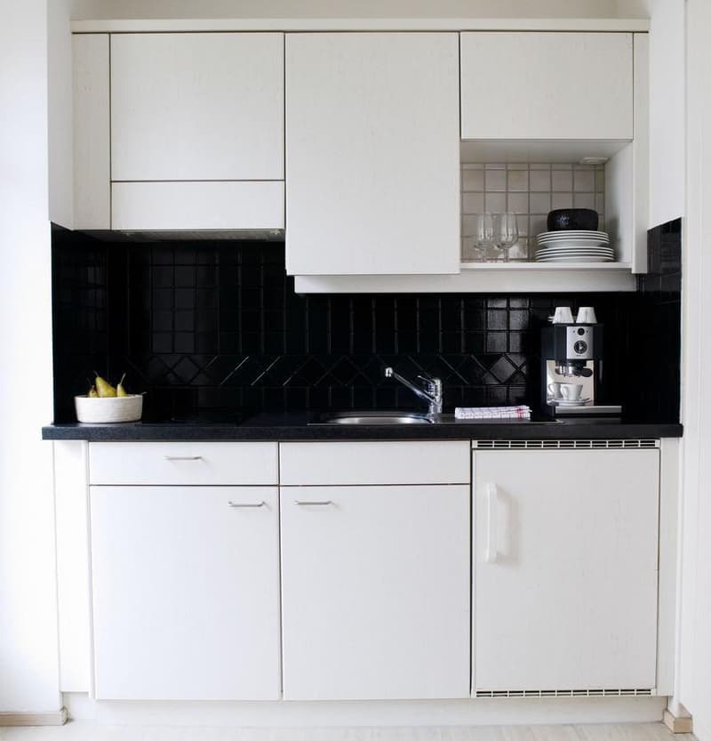 modern kitchen with white cabinets, black tiled countertop, integrated sink, stainless steel faucet, espresso machine, refrigerator