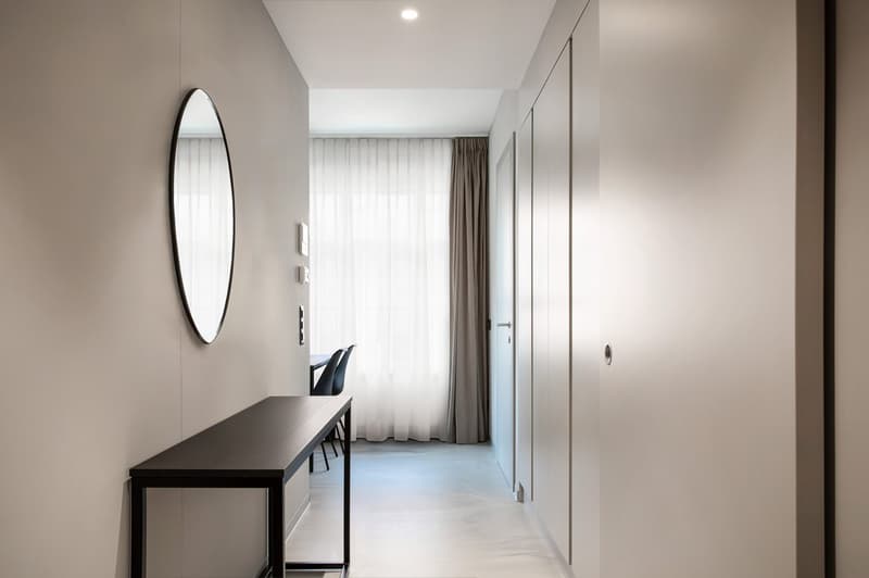 hallway with mirror, white walls, wooden flooring, desk and chairs, white curtains