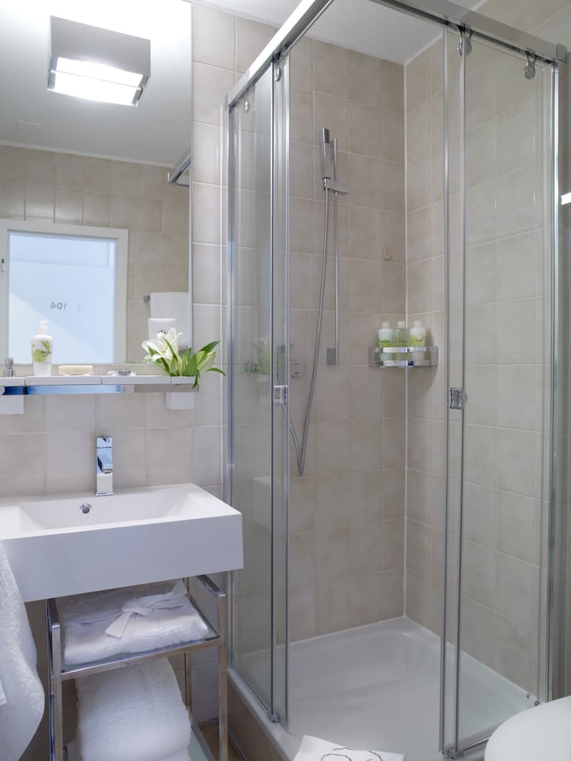 A modern bathroom with a white vanity, shower enclosure, and tiled walls.