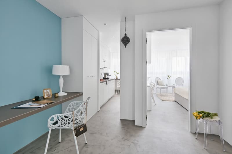 Minimalist decor, blue accent wall, white desk, white chair, white lamp, clear plastic stool, gray floor