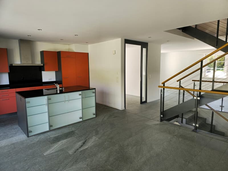 Modern kitchen with black countertops, glass cabinets, and red cabinets. Stainless steel stove and oven. Open space with staircase.