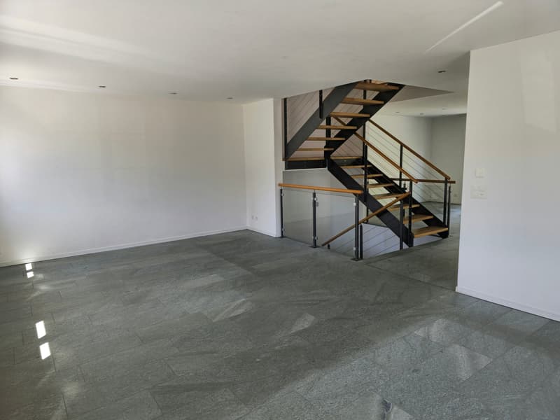 Empty room with white walls, gray tiled floor, and a modern staircase with a metal handrail.