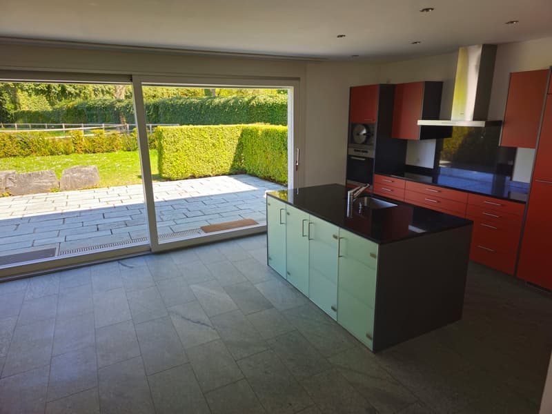 Modern kitchen with a large island, black countertops, green cabinets, and a sliding door leading to a patio.