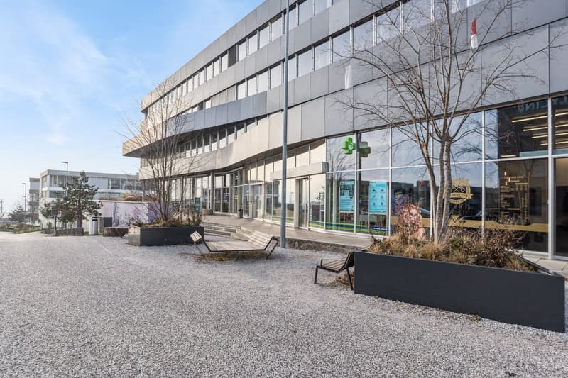 modern office building, glass windows, gray exterior, landscaped area with trees and benches