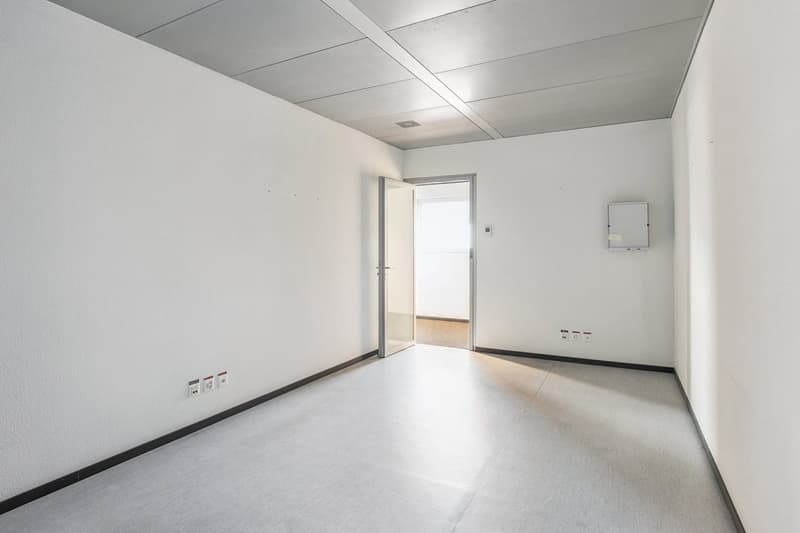 Empty room with white walls, ceiling, and flooring. There is an open door leading to another room.