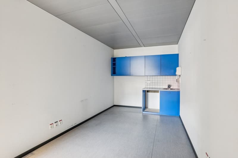 Empty room with white walls, blue cabinetry, open sink area with sink and small cabinet