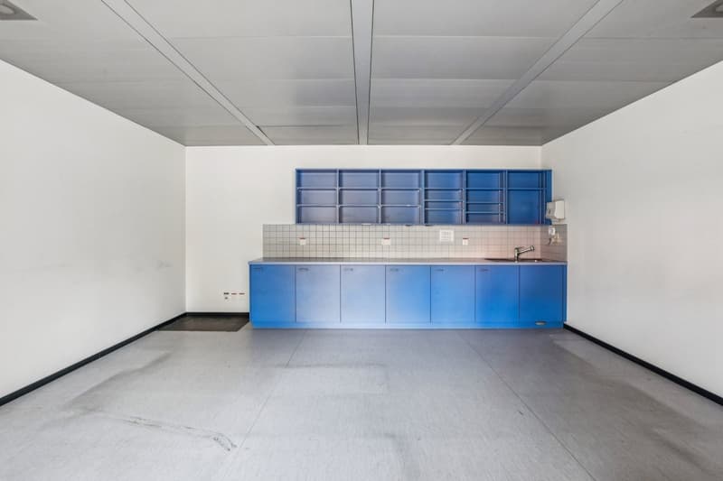 empty room with white walls, blue cabinets, tiled wall with a sink and faucet, ceiling with square panels, power outlets on the wall