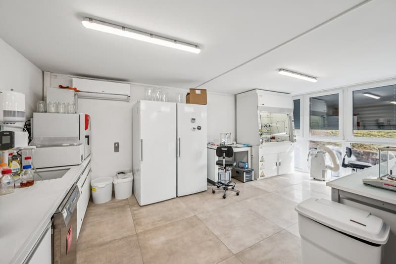 modern kitchen with white cabinets, tile flooring, countertop, two fridges, washing machine, trash bins, several electrical appliances and bottles on countertop