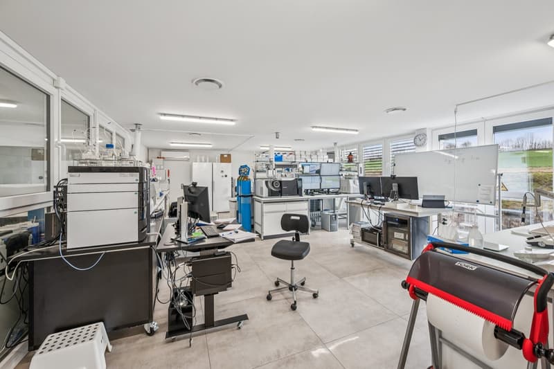 Well-lit office space with multiple desks, computer monitors, and various scientific equipment.
