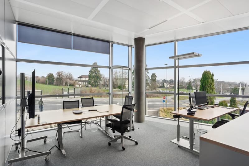 modern office with large windows, desks, chairs, computer monitors, and a view of the outside