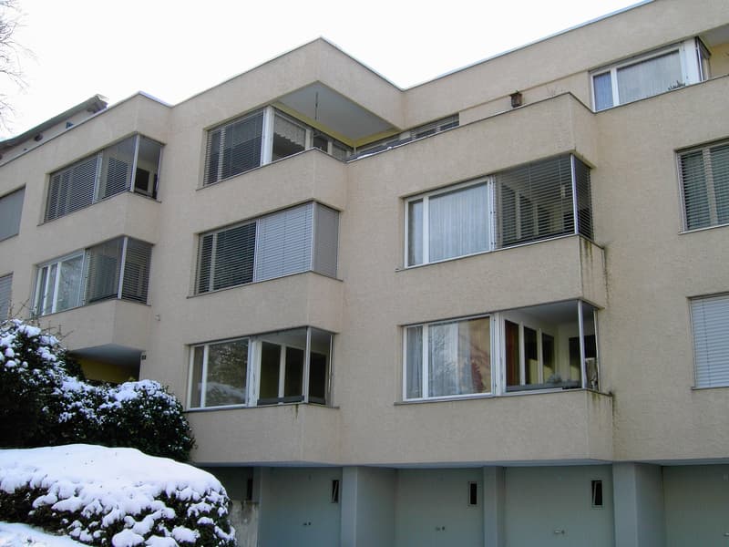 3 story apartment building, beige exterior, large windows, balconies, covered parking entrance