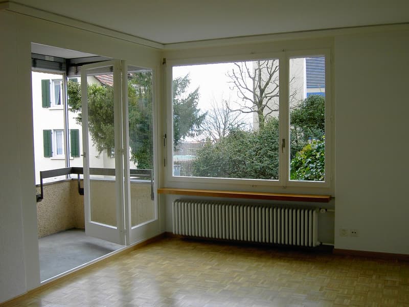 empty room, hardwood floors, large windows, balcony with a view of trees and another building