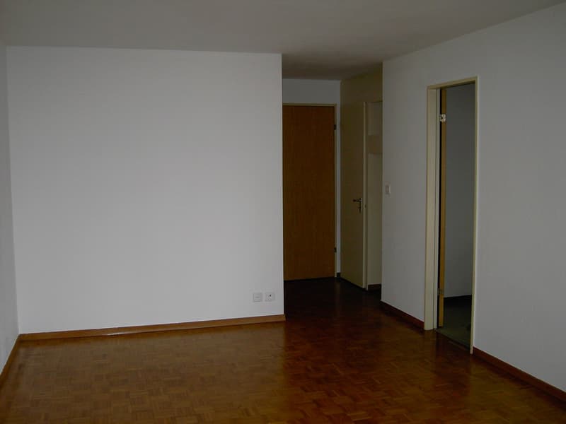 empty room with white walls, wooden flooring, power outlets on the wall, and three open doors leading to other rooms