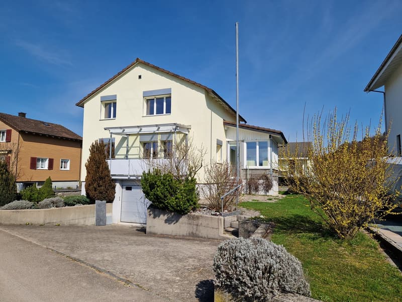 2 story house, yellow exterior, brown roof, garage, balcony, driveway, garden