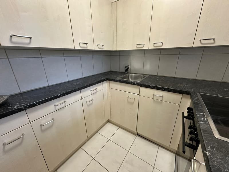 Compact kitchen with white cabinets, black granite countertops, tiled backsplash, and a stainless steel sink. The kitchen appears to have a dishwasher installed.