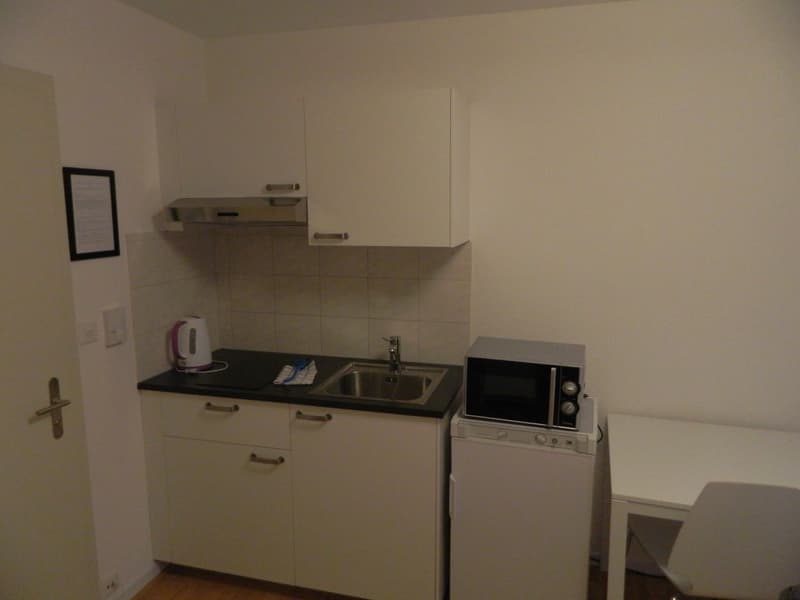 Small kitchen with white cabinets, black countertop, sink, microwave oven, and washing machine