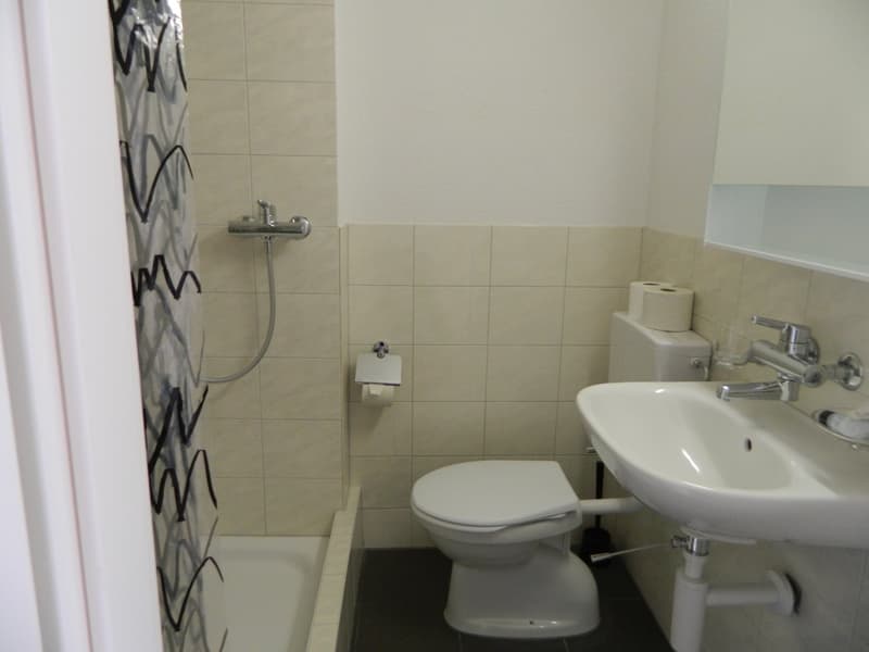 Bathroom with beige tile walls, toilet, sink, and shower area with a shower curtain.