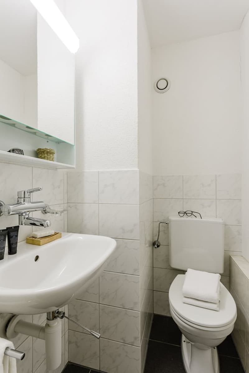 Tiled bathroom with a sink, toilet, and shelving above the sink