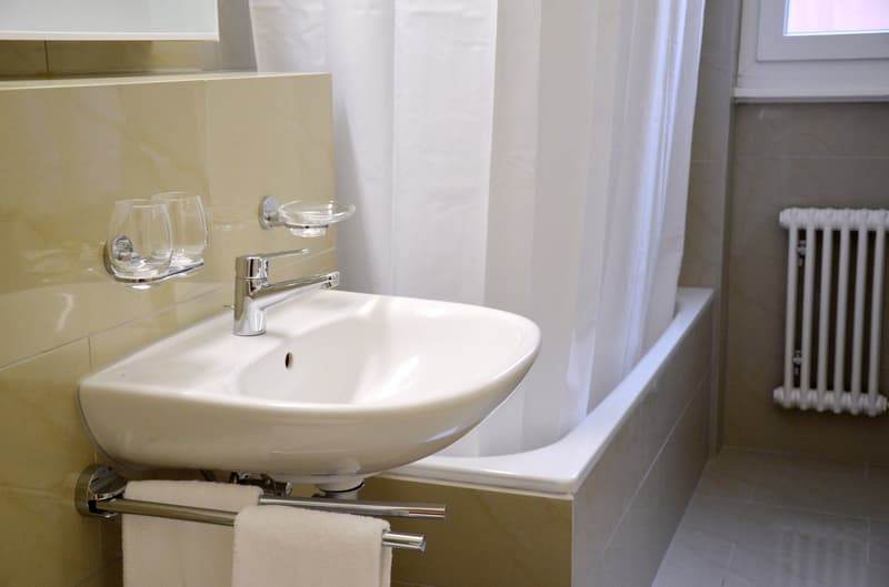 Bathroom with a white sink, chrome faucet, and towel rack. The walls are tiled in a light color and there is a radiator visible.