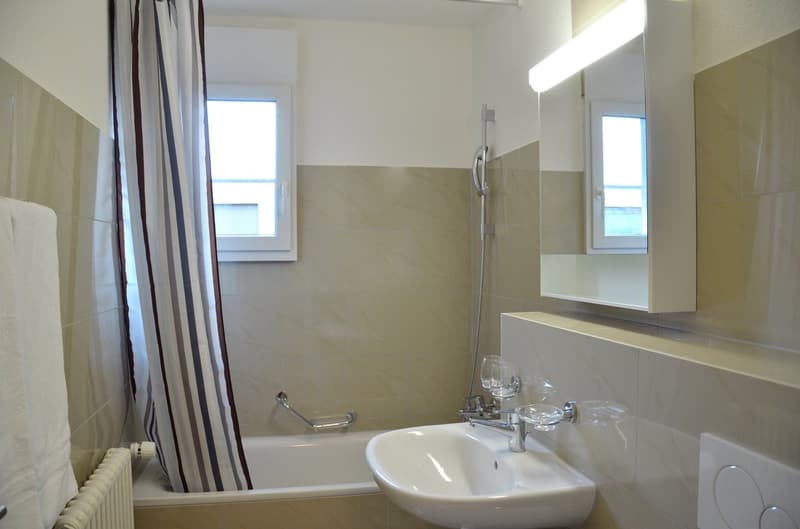 Tiled bathroom with a bathtub, sink, and shower curtain. The bathroom has a mirror and appears to be well-lit.