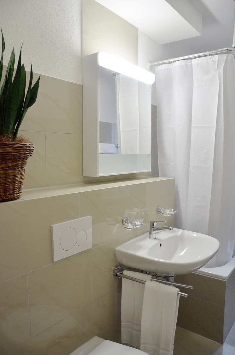 Modern bathroom with white tiles, a pedestal sink, a shower curtain, and a built-in cabinet above the sink.