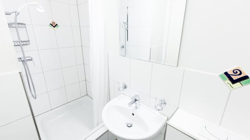 White tiled bathroom with a shower stall, sink, and bathroom accessories