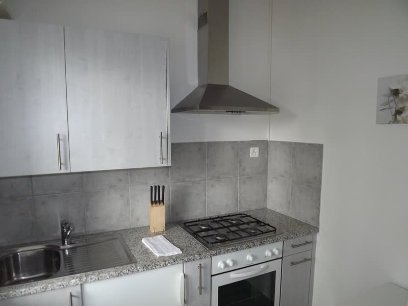 A kitchen area with white tiled wall, grey tiles floor, stainless steel sink, gas stove, and built-in oven.