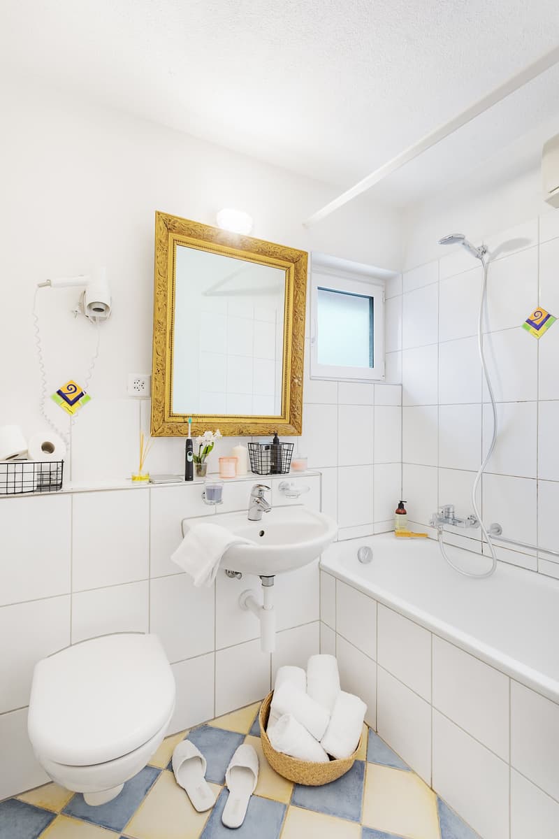 Bathroom with white tiles, bathtub, sink, and golden mirror