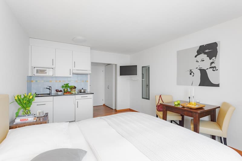 modern minimalist bedroom with a double bed, a small dining area, a kitchen with appliances and a sink