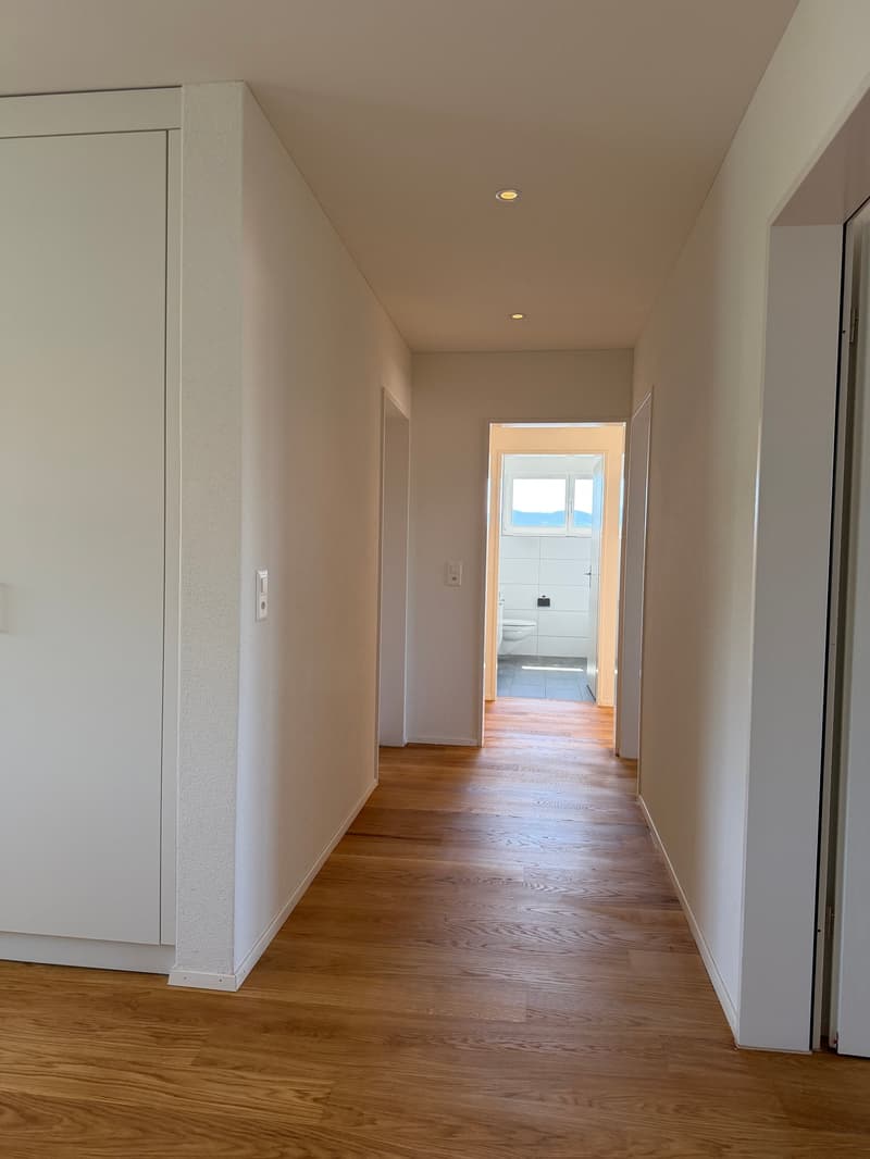 Empty hallway with wooden floors, white walls, and ceiling lights