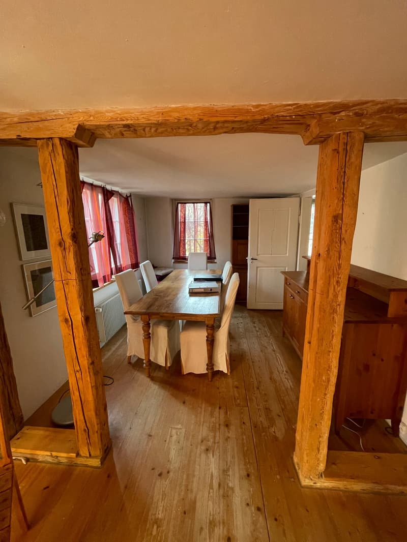 Dining room with wooden table and chairs, wooden pillars, wooden cabinet, white radiator, picture frames, wooden floor, open door