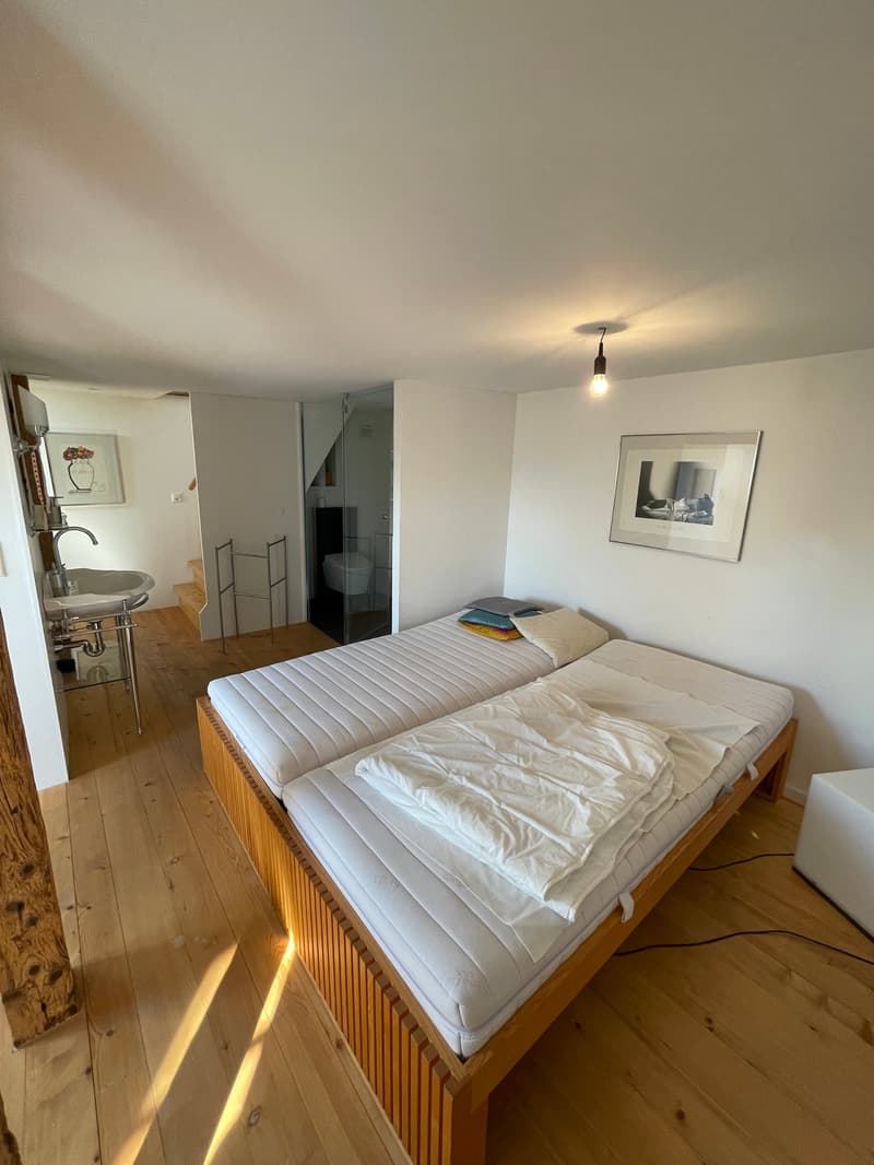 Two twin beds, clean and made, white sheets, bedside lights, bathroom door, open door leading to bathroom and hallway