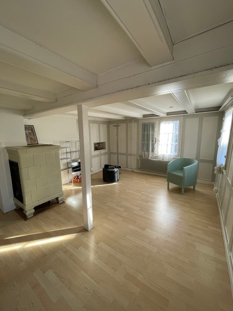 Empty room: hardwood floor, fireplace, window with white curtain, white wall, black modern armchair