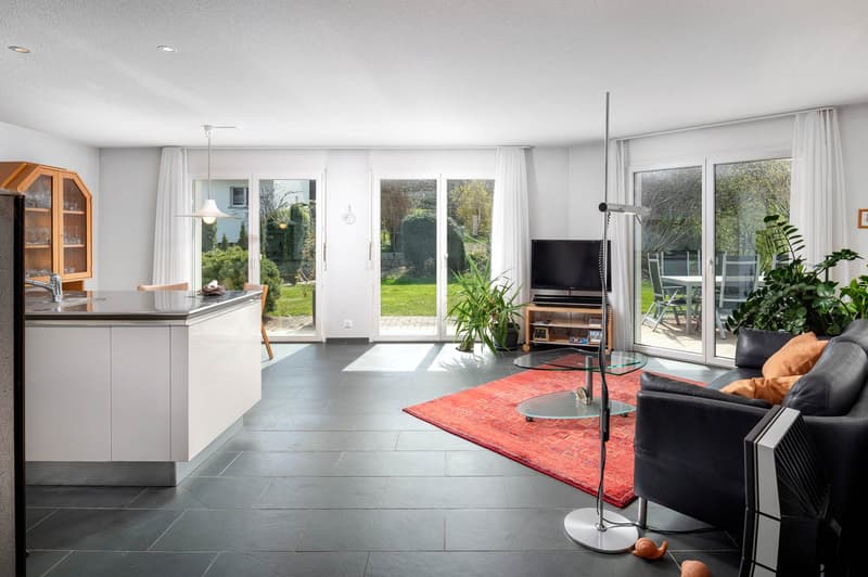 modern living room with large windows, sliding doors, black leather couch, red rug, glass table, TV, plants