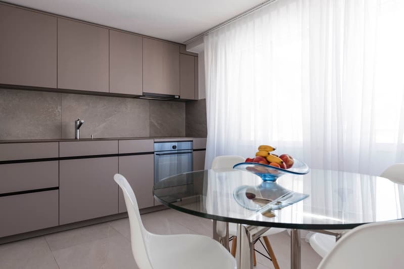 modern kitchen, gray cabinets, granite countertops, built-in dishwasher, integrated oven, gas stove, white chairs, glass table