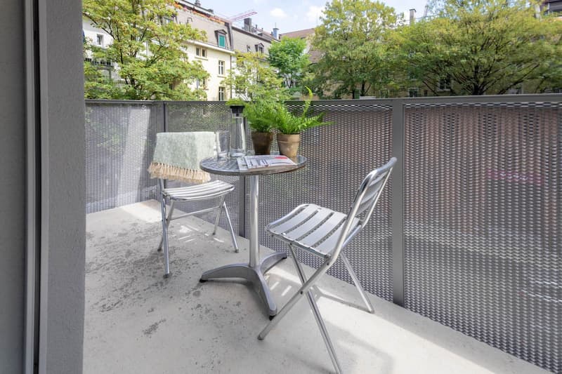 small balcony with 2 folding chairs, a round table, and potted plants, metal fencing