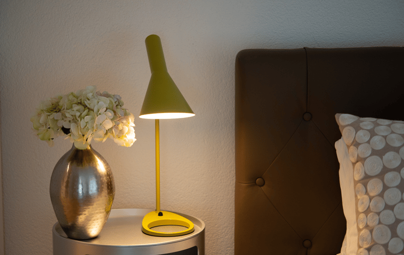 Bed with leather headboard and dotted pillow, nightstand with lamp and vase, white wall