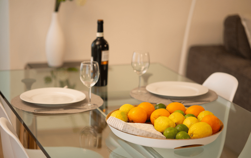 Glass table, white plates, wine glasses, wine bottle, fruit bowl