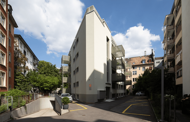 Modern apartment building with raised ground floor, balconies, garage, and parking places