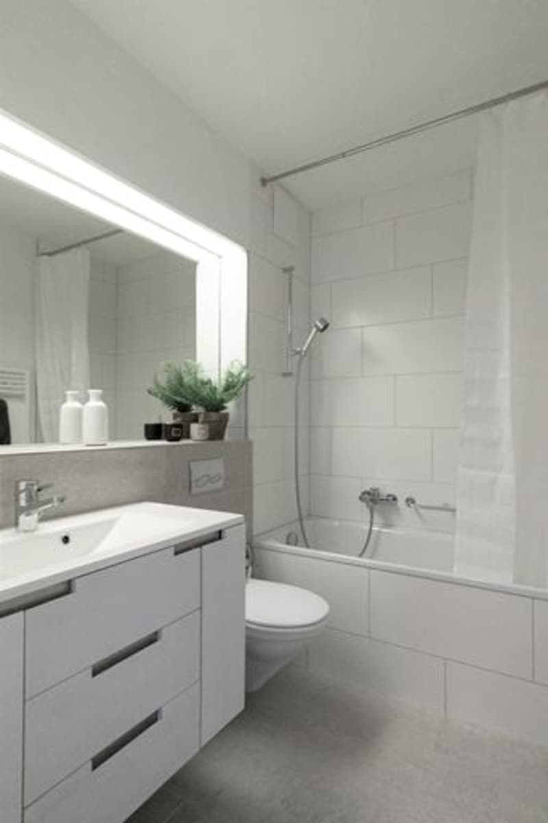 Modern, minimalist bathroom with white tiled walls, white cabinetry, under-mounted sink, shower enclosure with glass door, modern fixtures, ceramic floor, full-length mirror, plants on the windowsill.