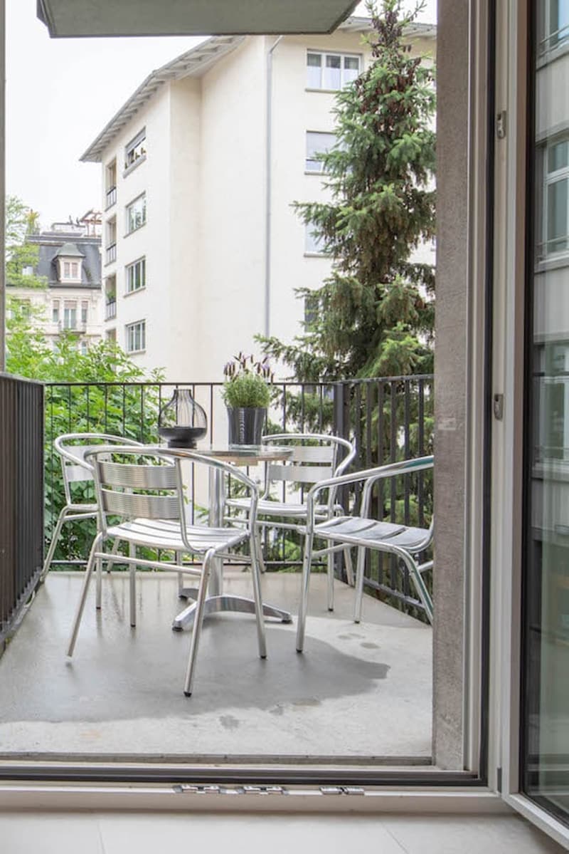 A balcony with a small table, four chairs, a plant and a lantern