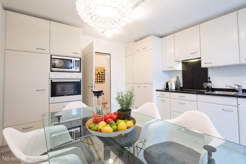 white kitchen, white cupboards, silver appliances, glass dining table, chairs, chandelier, bowl of fruits