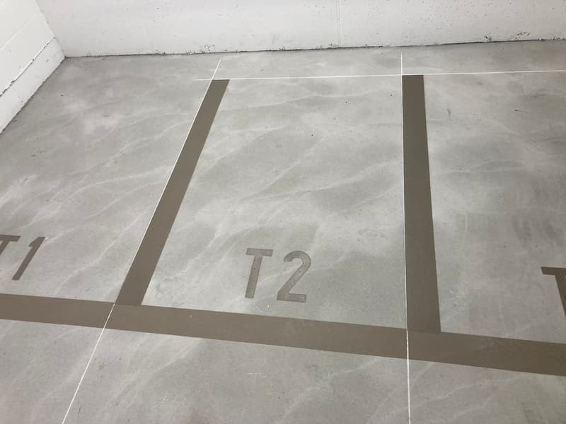 Underground parking area with white and gray painted walls, gray floor with parking spaces indicated.